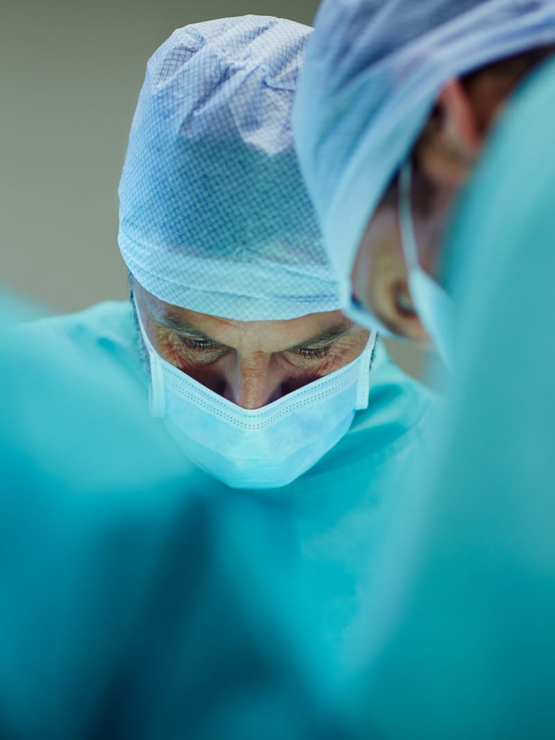 Two male doctors in scrubs and facemasks looking down over their work