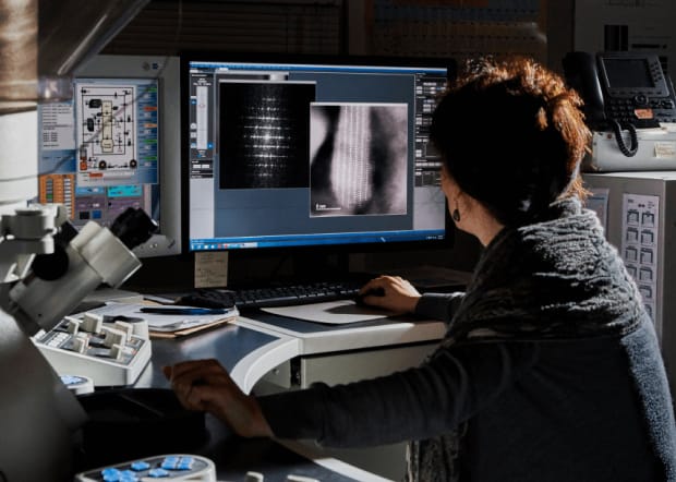 Woman working on a computer with lab equipment surrounding her