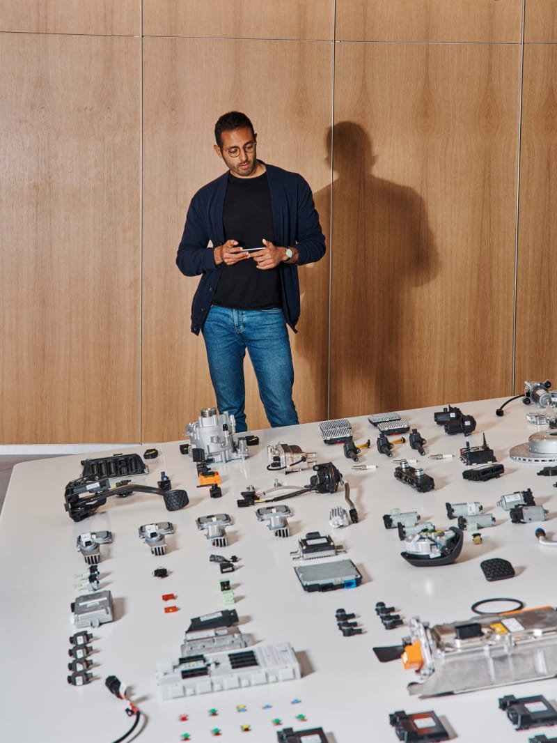 Man holding a cell phone and standing in front of a table covered in parts